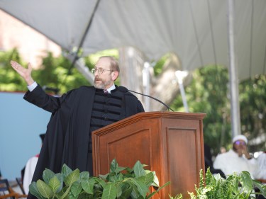 Alan Garber stands at a podium with his arm extended outward.