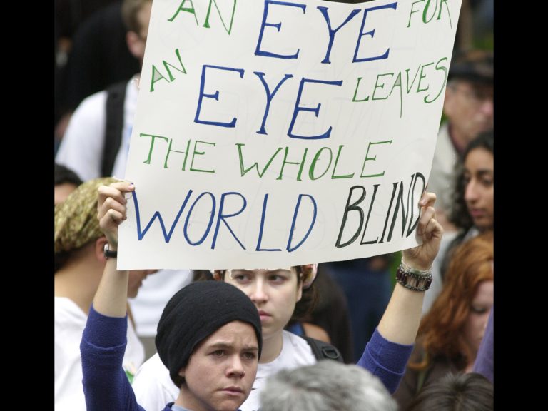 A woman holding a sign that says "An eye for an eye leaves the whole world blind"