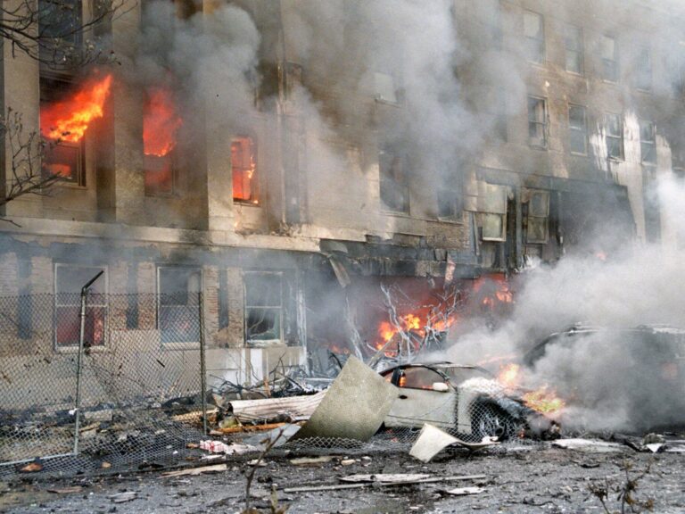 A street with a crushed car and a building on fire